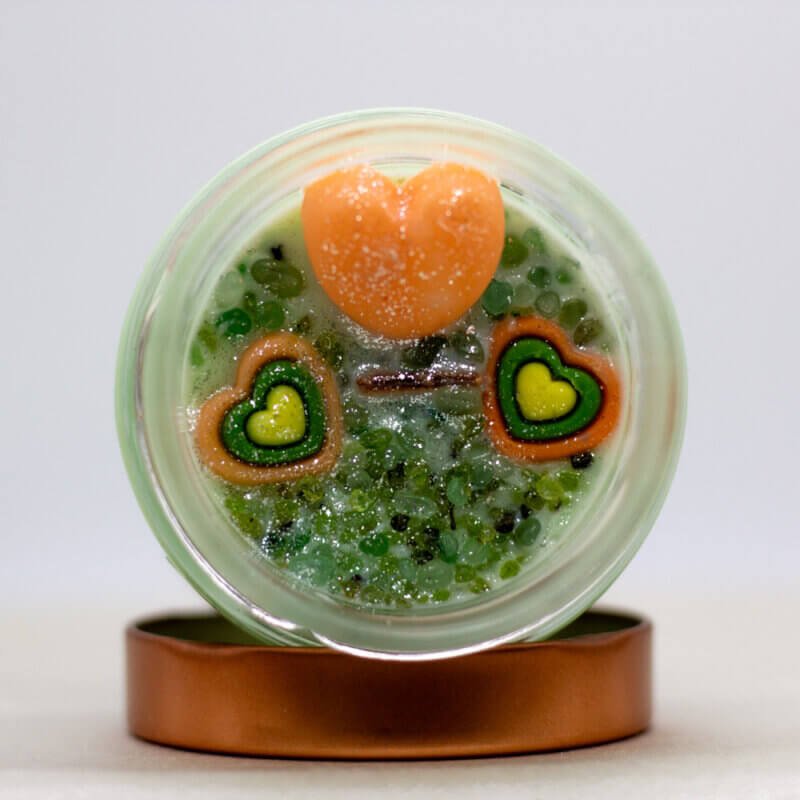 Solminea candle with peridot and green aventurine crystals on top, sparkling with light and surrounded by fresh greenery.
